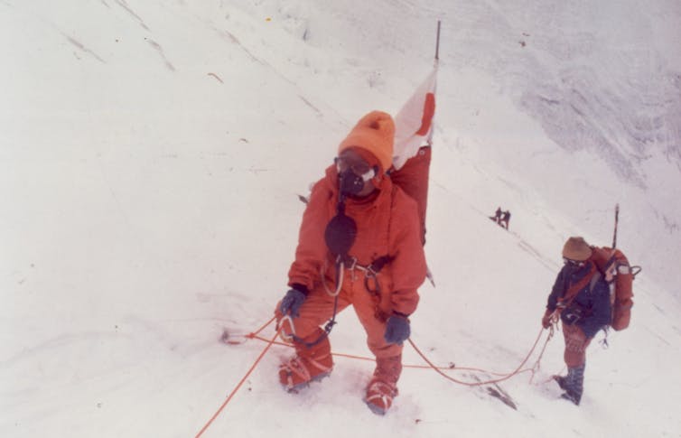 Junko Tabei, dressed in orange with her face covered by an oxygen mask, and a companion climbing Everest