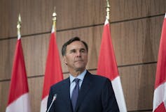 El hombre de cabello oscuro en las suites se encuentra frente a una serie de banderas canadienses.