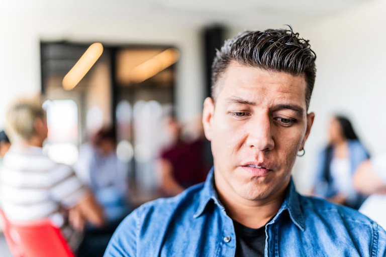 With a group of people in the background, a worried-looking, dejected man faces the camera.