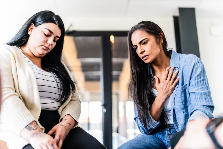Two unhappy-looking women, with eyes cast downward, look forlornly at the floor.