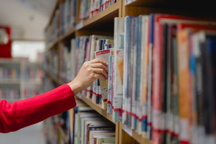 A hand picking a book off a library shelf