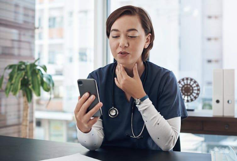 Doctor motions to throat during videocall