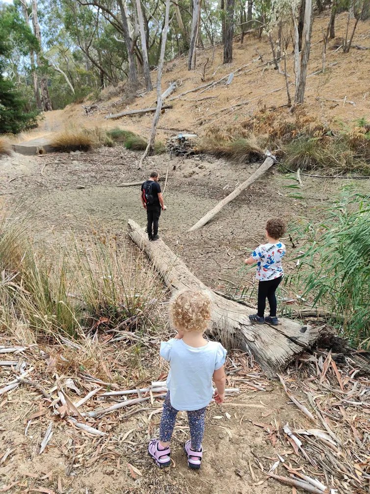 Two young children and a man inspect a dry waterhole on private property in the AdelaideHills, March 2025.