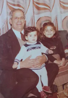 A family photo of an older man holding a toddler, with a young girl sat beside them.