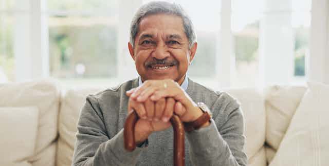 A man with gray hair and a mustache smiling and holding a cane