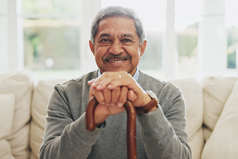 A man with gray hair and a mustache smiling and holding a cane