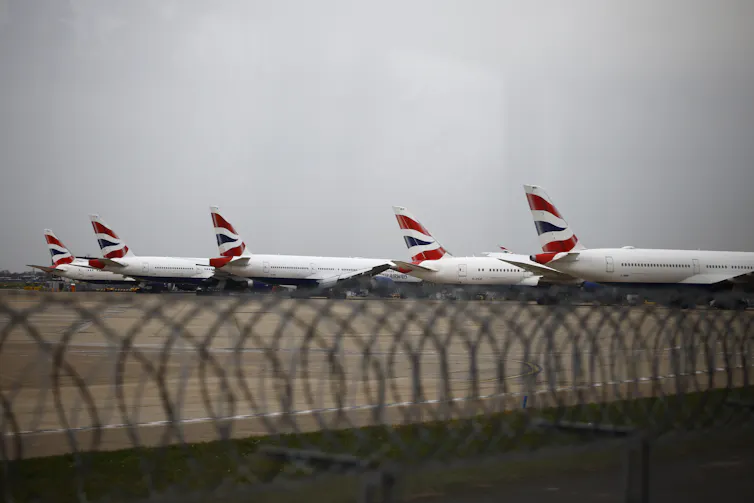 Row of aeroplanes with British flag design on tails, behind razor wire fence