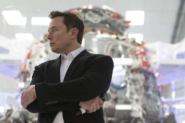 Elon Musk at SpaceX headquarters, with his arms crossed.