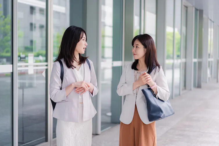 Two women speak to each other outside of a building.