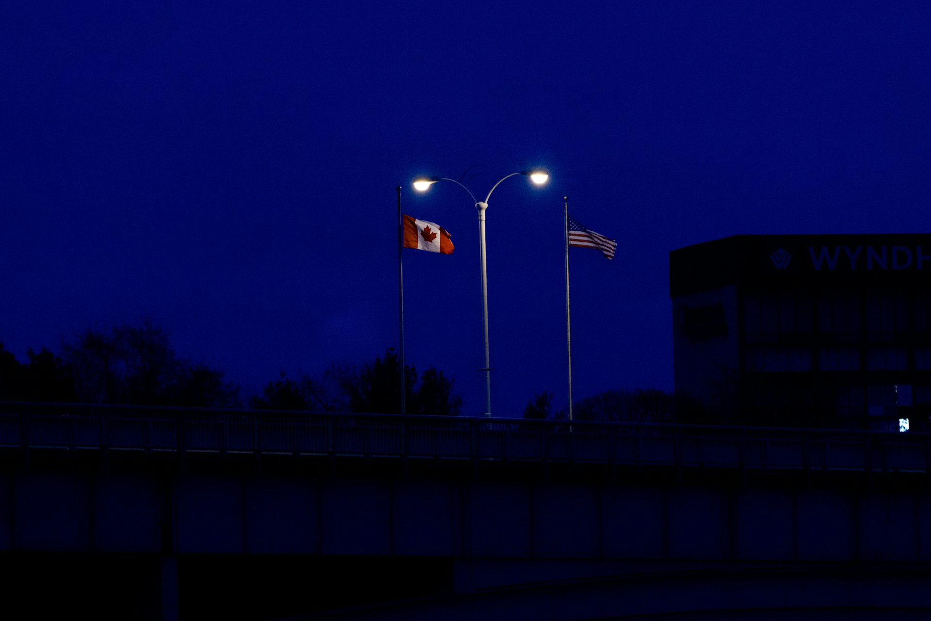 Flag with maple leaf and flag with stars and stripes spotlit by lights at night.