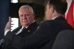 A man in suit listens to another man who gestures.