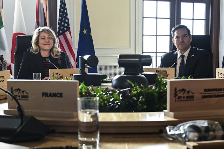 Two people at a table with laptops in front and the U.S. flag seen in background.