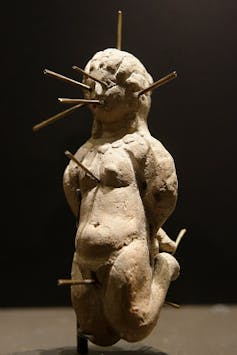Muñeca vudú perforada con trece alfileres, encontrada en un jarrón de terracota con una tablilla de plomo con un hechizo de atadura.