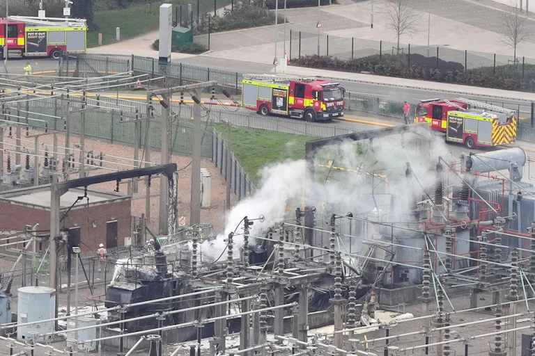 Smoke rising from large installation of electrical equipment with fire engines nearby