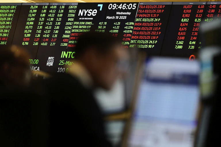 Stock market numbers displayed on a screen behind the blurred image of a person working on the options floor