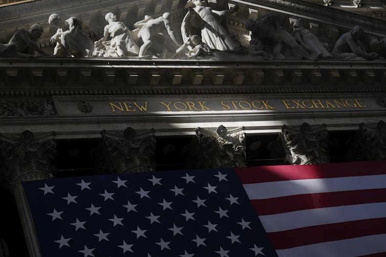 An American flag seen in front of a building that says 'New York Stock Exchange'