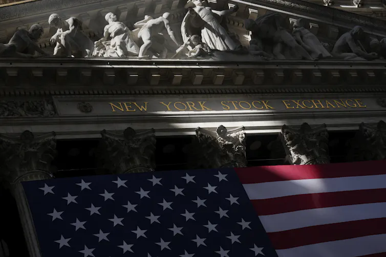 An American flag seen in front of a building that says 'New York Stock Exchange'