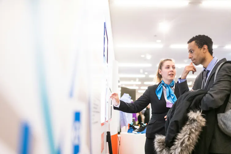 A woman points to a info on a wall while a man looks on a listens