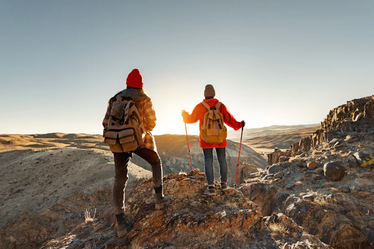 Two young hikers girls are standing at sunset cliff and looks at the view