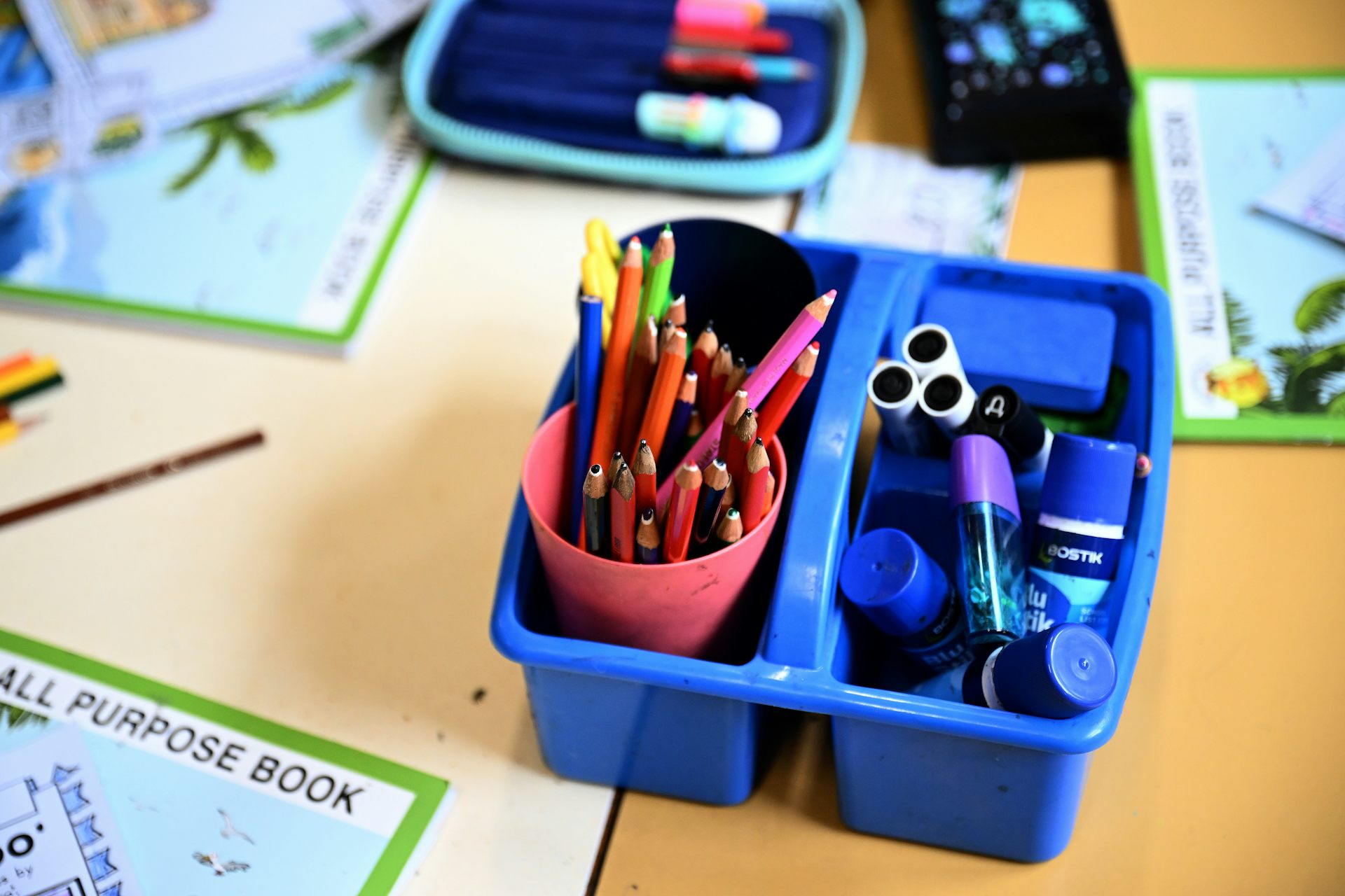 A container of pencils, glue and supplies on a classroom desk.