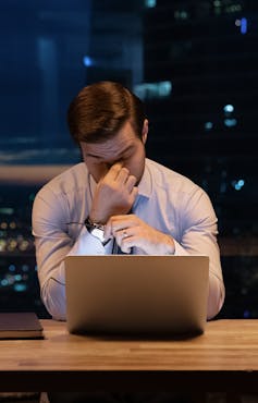 Overworked young man rubs eyes looking at laptop