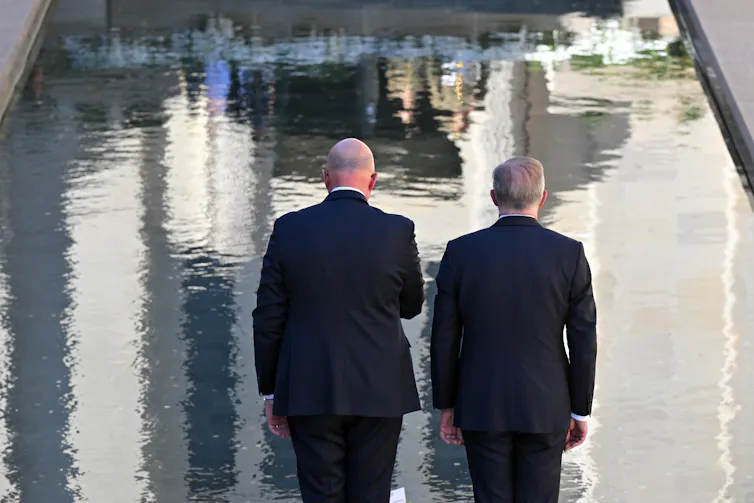 Albanese and Dutton face away from the camera and stare desolately at a body of shimmering water.