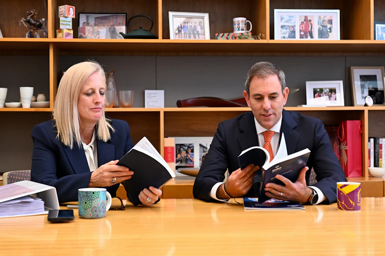 A woman and a man sit at a desk and flip through books