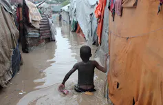 A child wades through brown water up to his waist after a flood has swept through a refugee camp