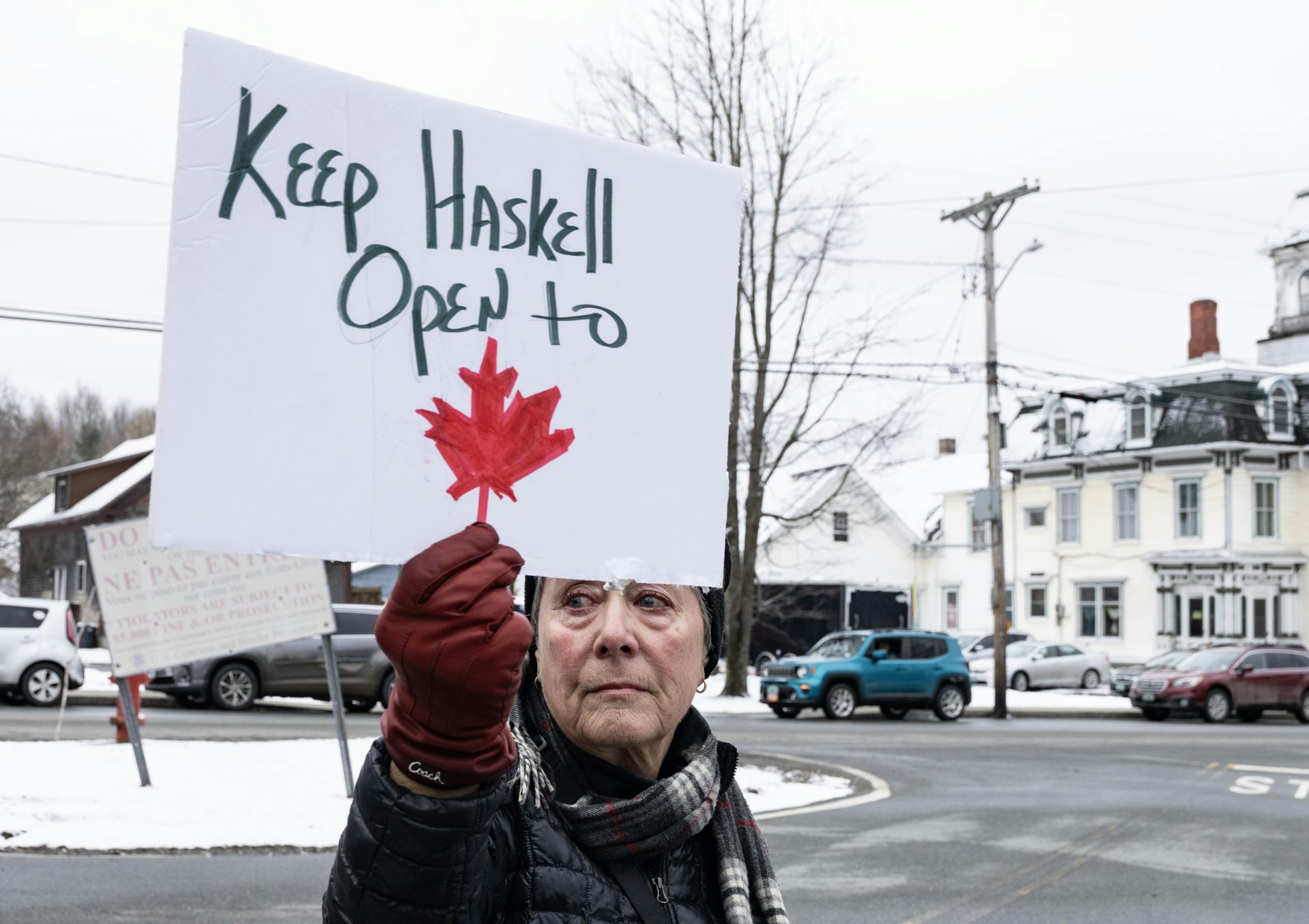 A woman holds a sign that reads Keep Haskell Open to Canada.