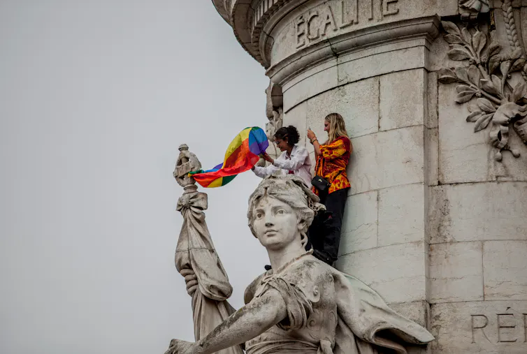 Two women waving a flag from a statue in France.