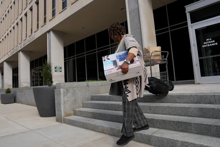 Woman walks out of a government building holding boxes of belongings