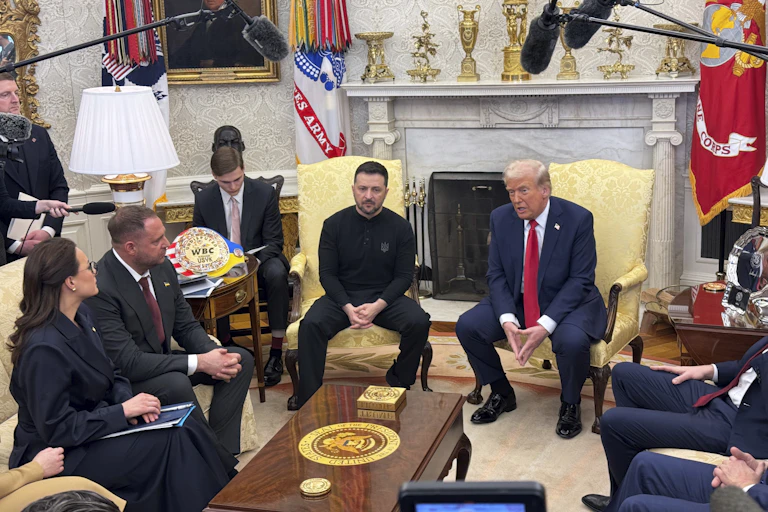 Two sit in an an ornate office with media around them.