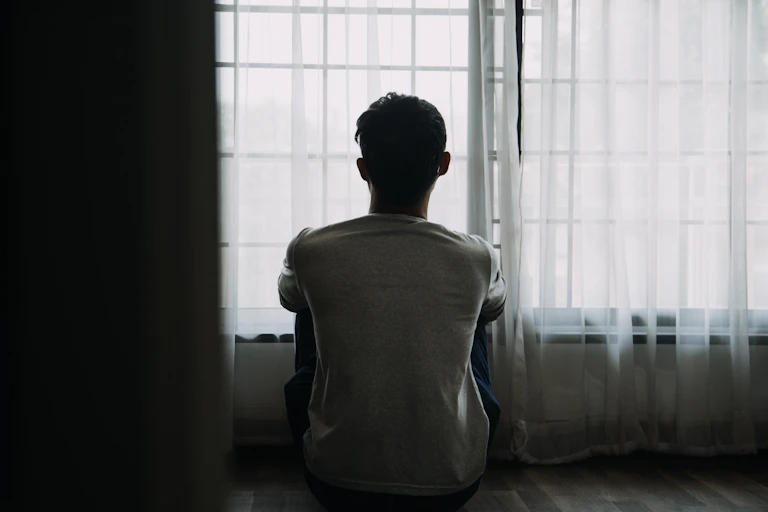 young man sitting alone staring out of a window