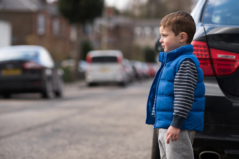 A boy crossing the street between parked cars.