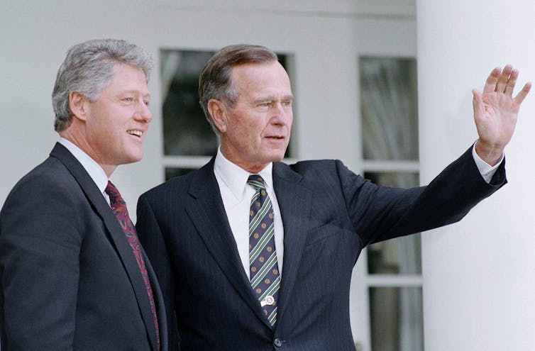 Bill Clinton smiles as George H. Bush waves to the crowd.