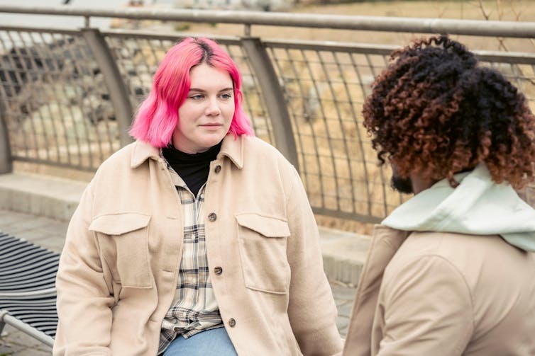 Two women in light jackets outdoors having a conversation.