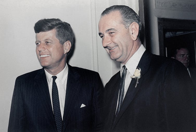 Kennedy and Johnson in identical black suits and white shirts.