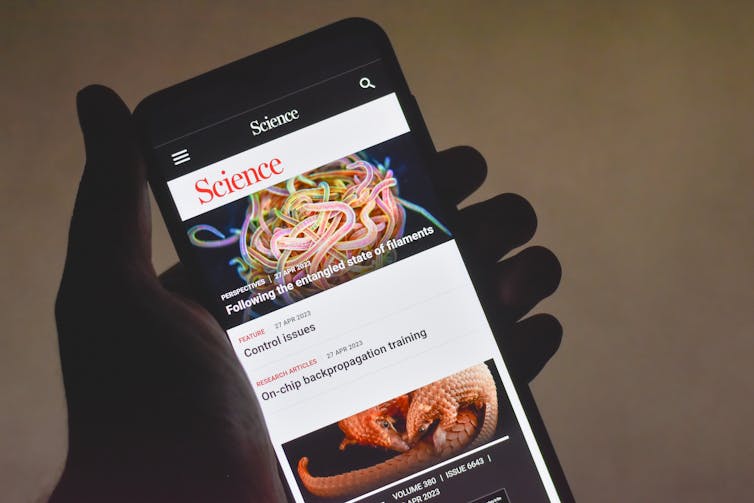 A hand holding a mobile phone displaying the Science journal home page.