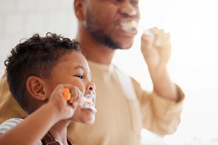 Little boy and father brush teeth in mirror.