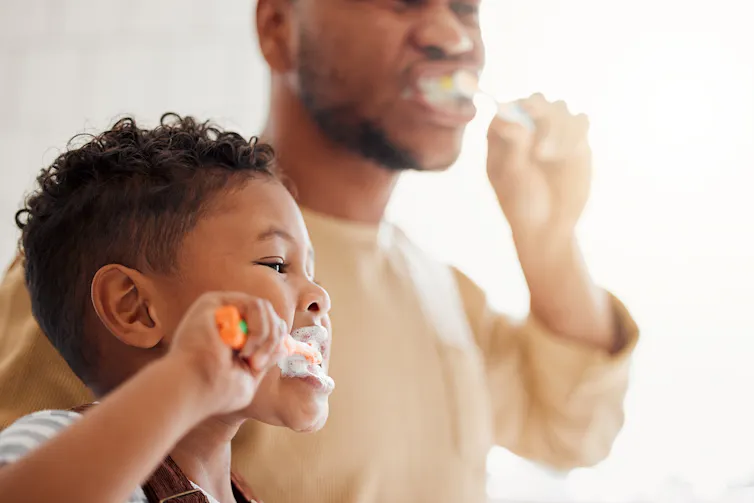 Little boy and father brush teeth in mirror.