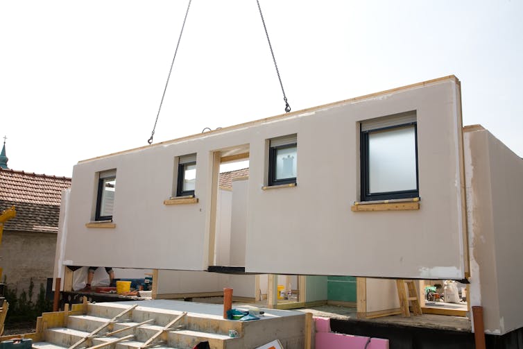 A crane lifts part of a modular home into place