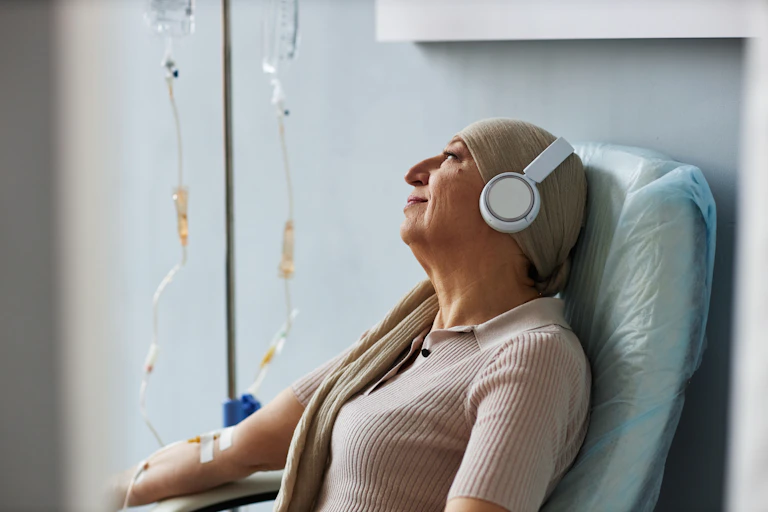 A woman in a headscarf listens to music while receiving an infusion.