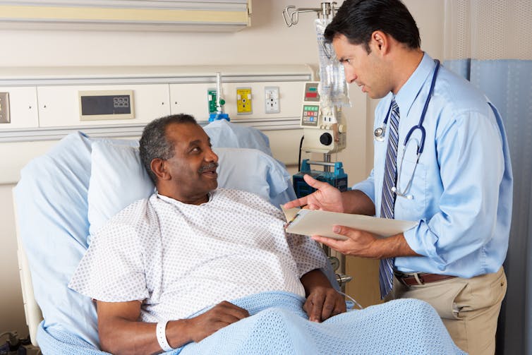 A man in a hospital bed is seen by a male doctor.