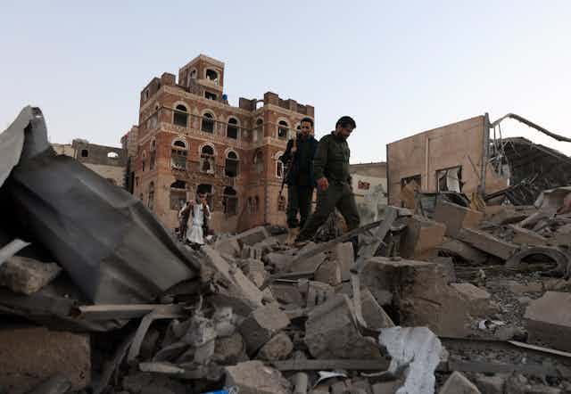 People holding guns walk through piles of rubble.