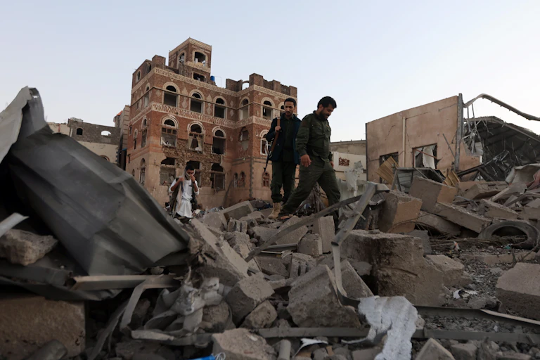 People holding guns walk through piles of rubble.