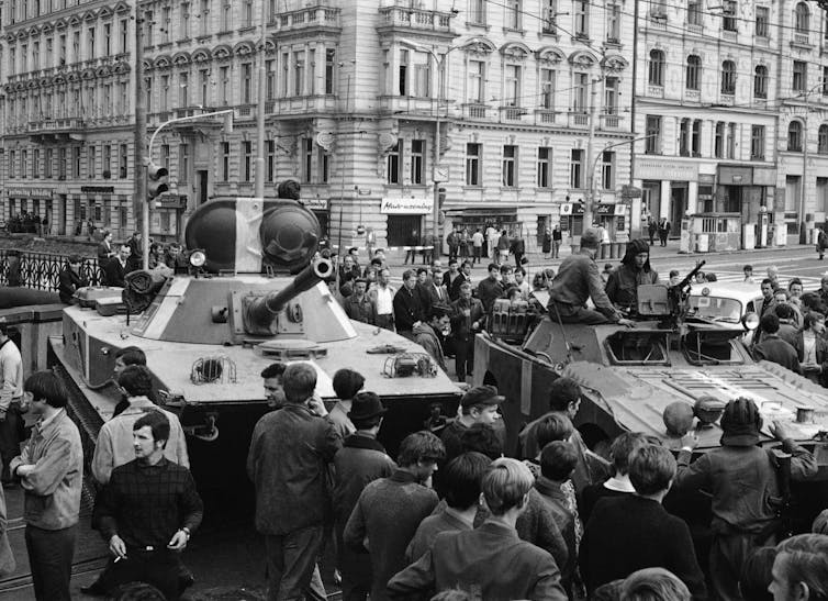 A black-and-white photos shows a Soviet tank in a city square surrounded by people.