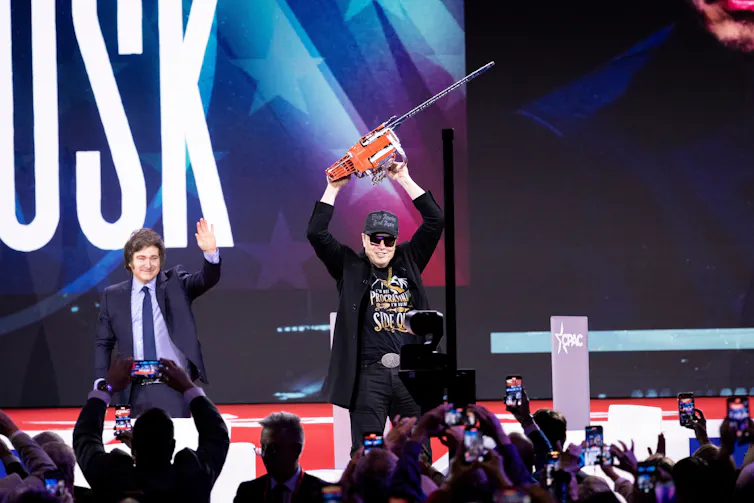 elon musk on stage with a chainsaw as argentinian president javier milei looks on.