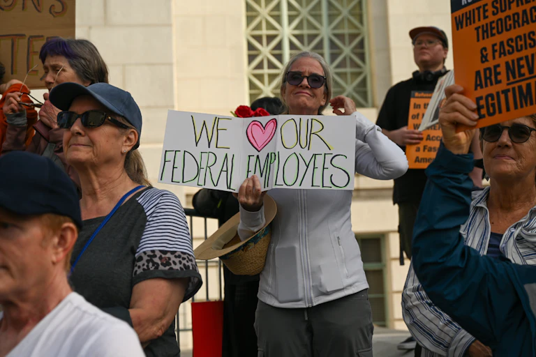 woman holds up a protest sign reading we love our federal employees