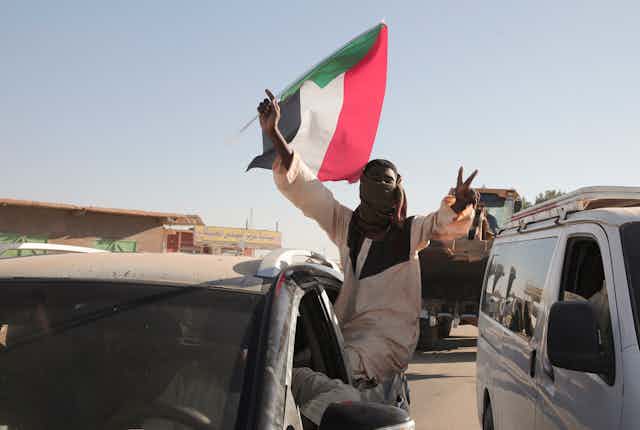 A man flashes victory V signs while holding a red, white, black and green flag.
