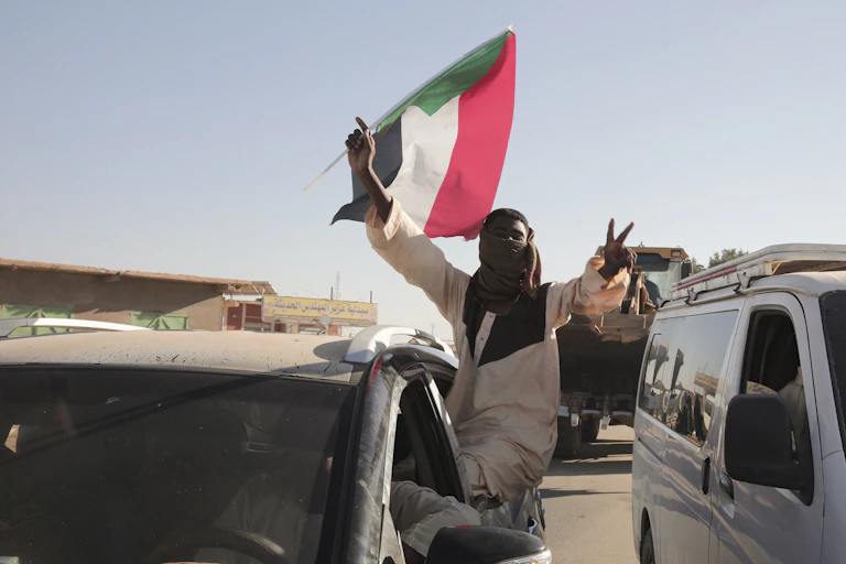 A man flashes victory V signs while holding a red, white, black and green flag.
